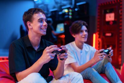 Two teen friends are playing a game console using gamepads and smiling while sitting on bean bags. Blue and red illumination - Agrandir l'image, fenêtre modale